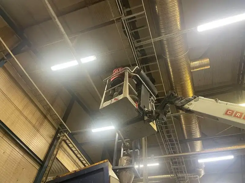 Töötaja korvtõstuki korvis tööstushalli lae all