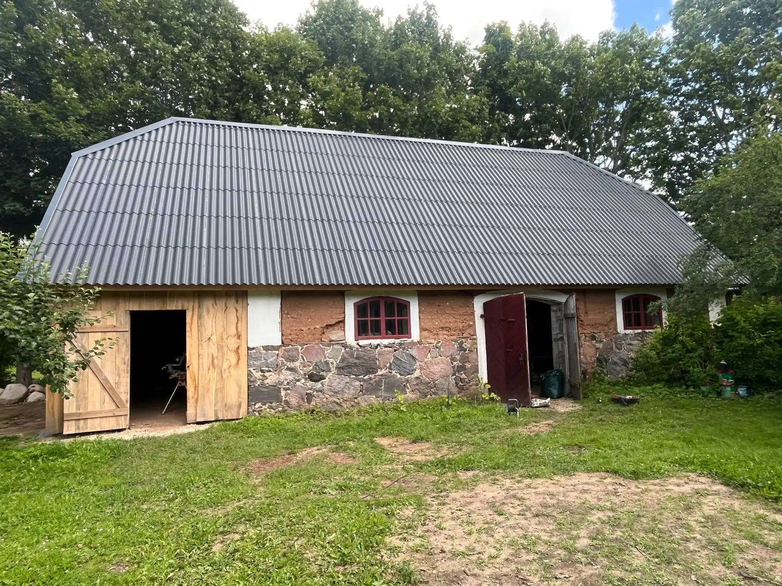 Old clay-walled building with a new metal roof, new doors and red arched windows